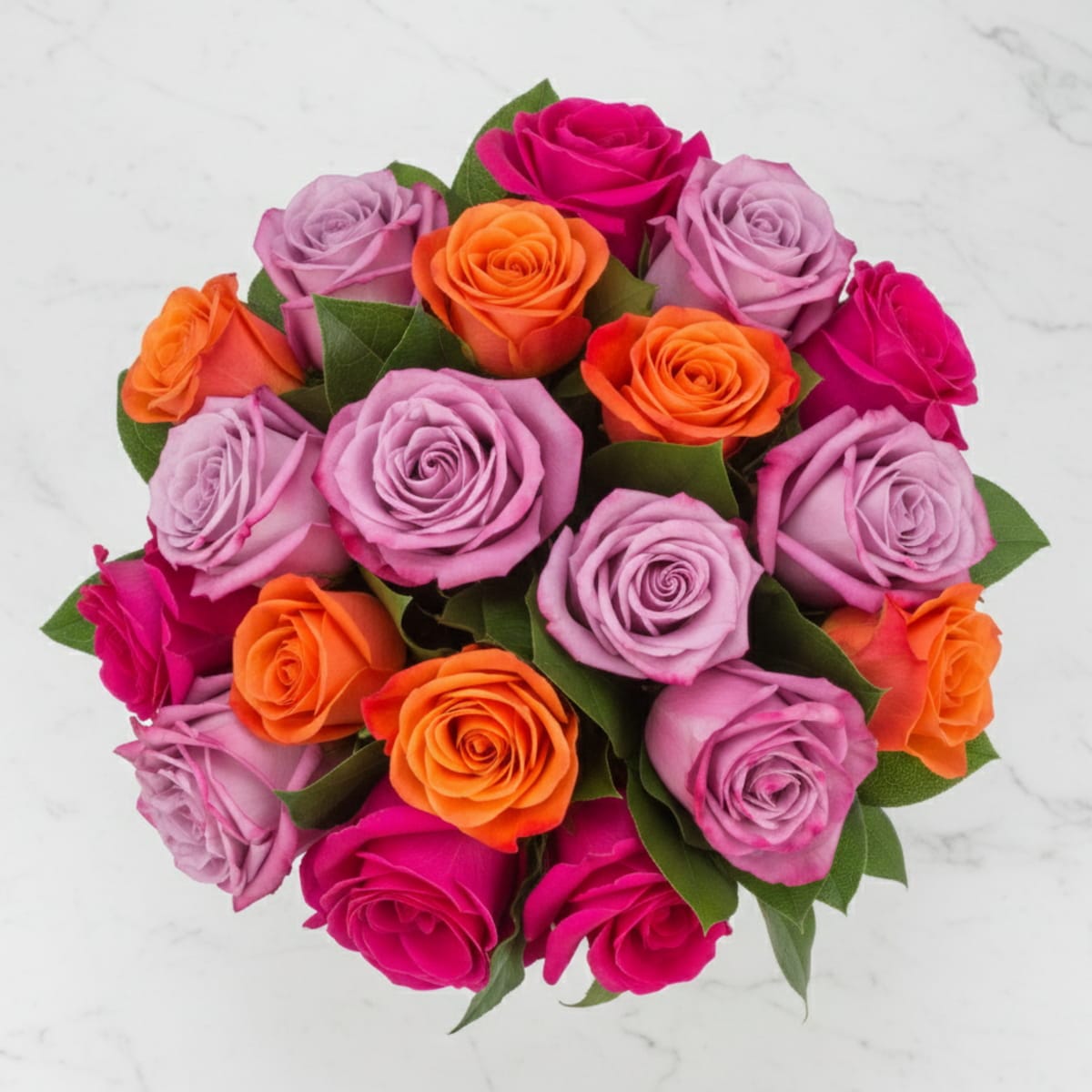 An overhead shot of a round bouquet featuring a beautiful mix of lavender, hot pink, and vibrant orange roses with green leaves, presented on a white marble background.