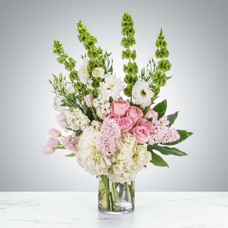 The Havencrest floral arrangement from Grace & Blooms in Naples, FL, featuring pink roses, white hydrangea, and green Bells of Ireland, representing luxury seasonal flowers.