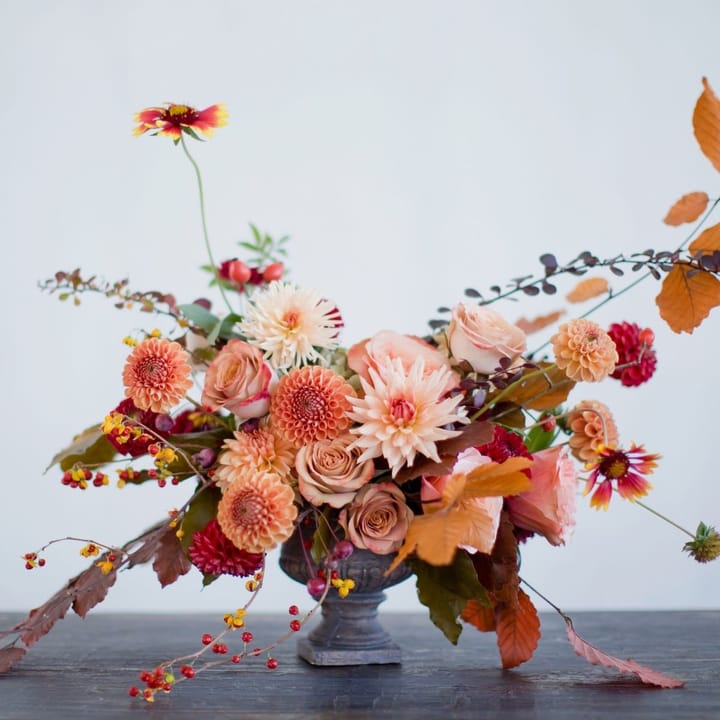 A luxury fall floral arrangement for a Naples, FL home, featuring terracotta dahlias and soft orange roses in a stone urn, representing the 2025 'Gulf-Kissed Hues' trend.