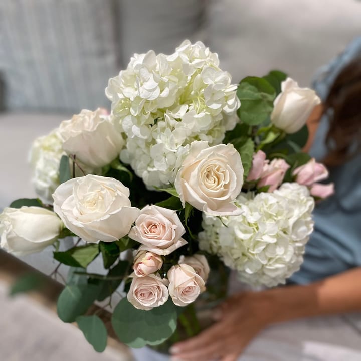 Emily, owner and head florist of Grace & Blooms Naples, sits on a couch holding a beautiful bouquet of white and pink flowers.