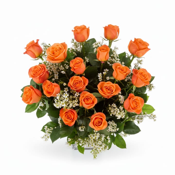 A professional floral arrangement of vibrant coral roses, delicate white wax flowers, and fresh green lemon leaf artfully designed in a clear glass vase, sitting on a clean white surface.